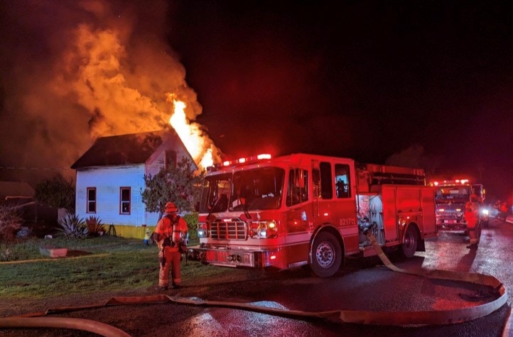 Firefighters and fire trucks at night, battling a house fire with visible flames.