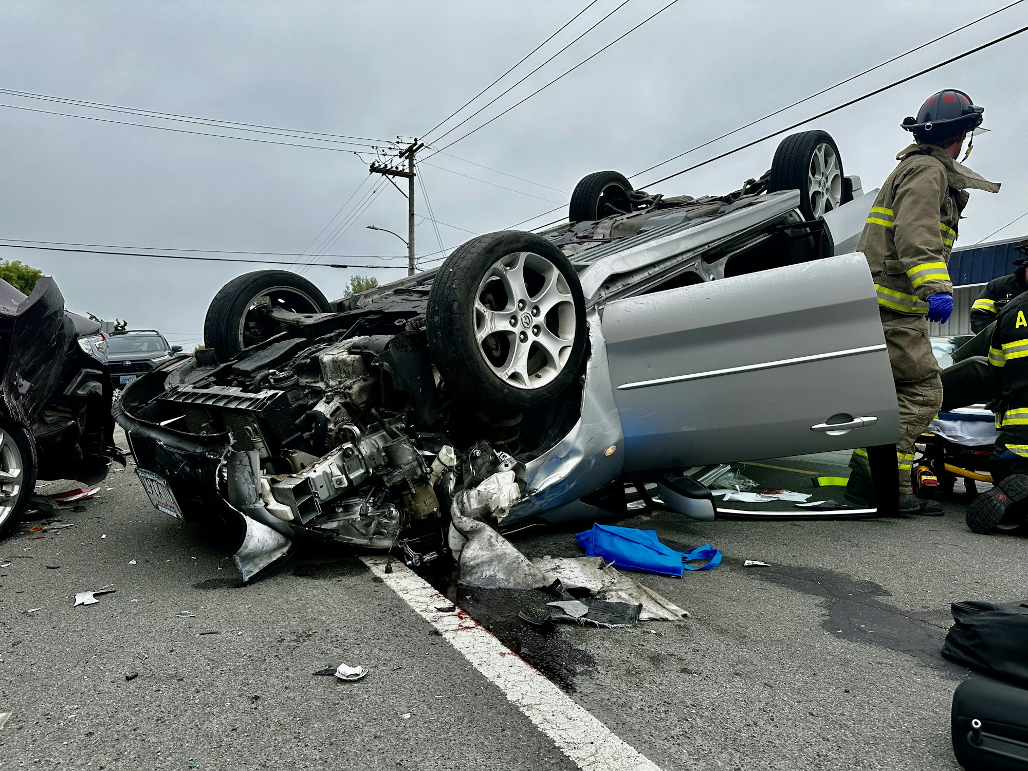 A flipped car after a crash with firefighters and debris around.