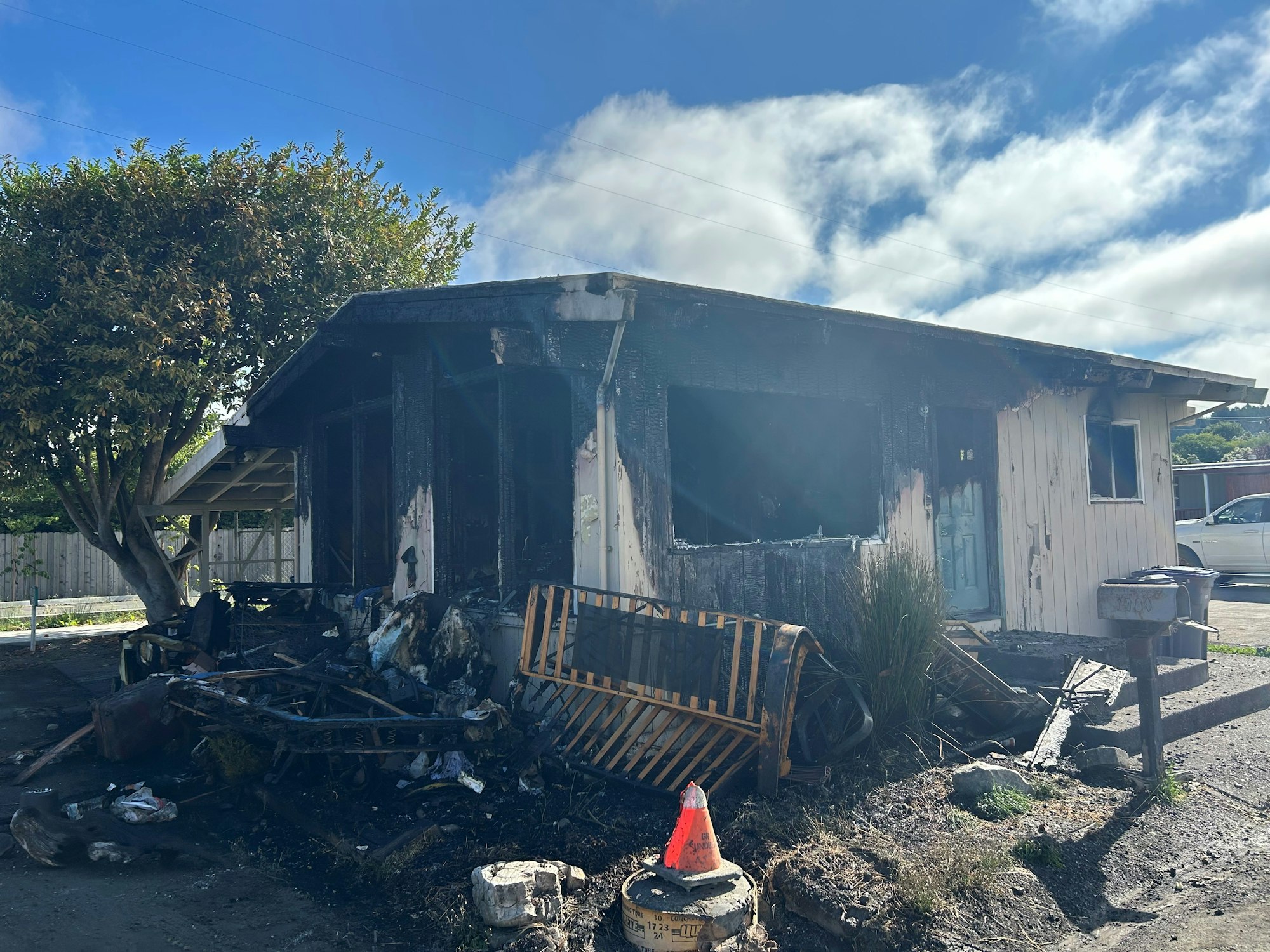 A burnt house with damaged items in front, under a blue sky.