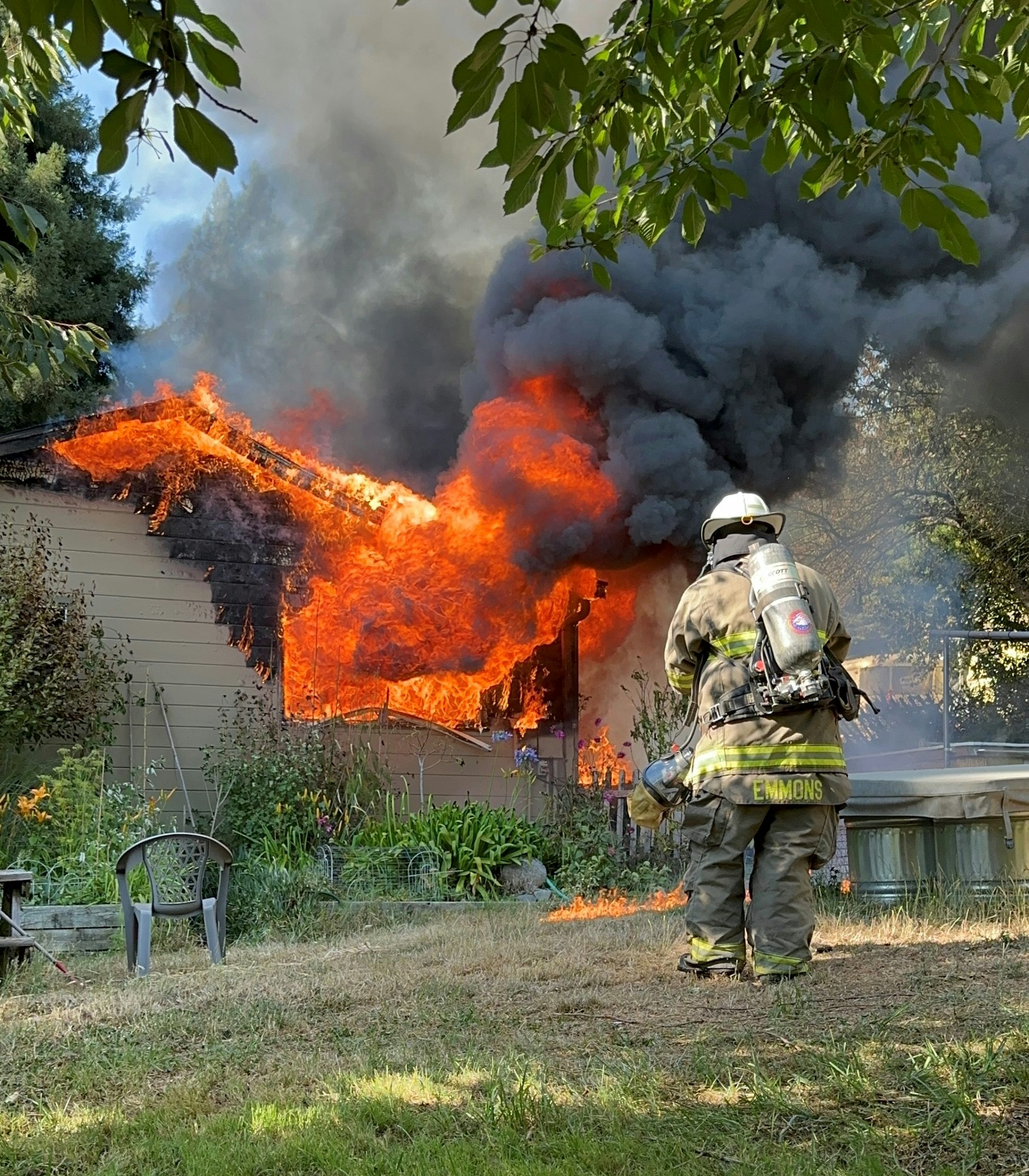 A firefighter observing a raging house fire with intense flames and smoke.