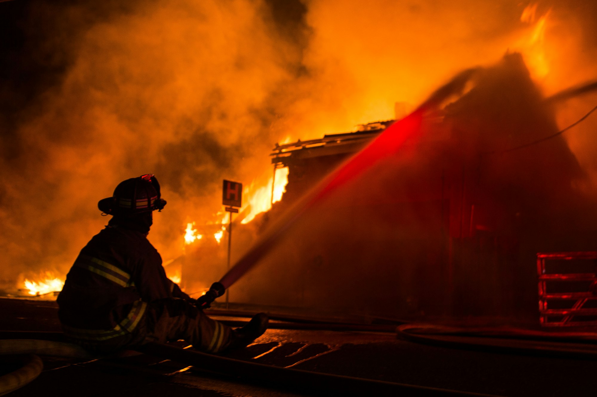 Color photo of a fire fighter directing a hose stream on a structure fire.