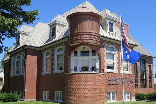 A historic red brick library building, with flagpoles and blue sky.
