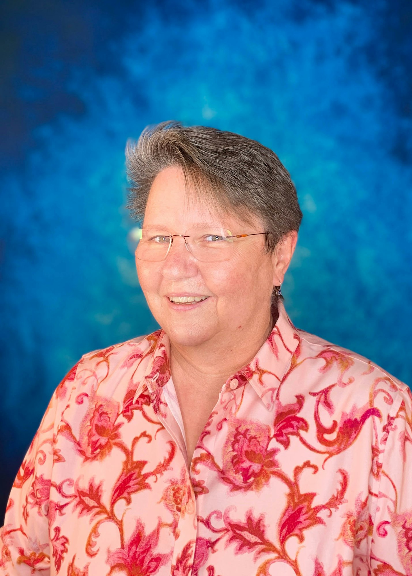 A person wearing glasses and a patterned shirt against a blue background.