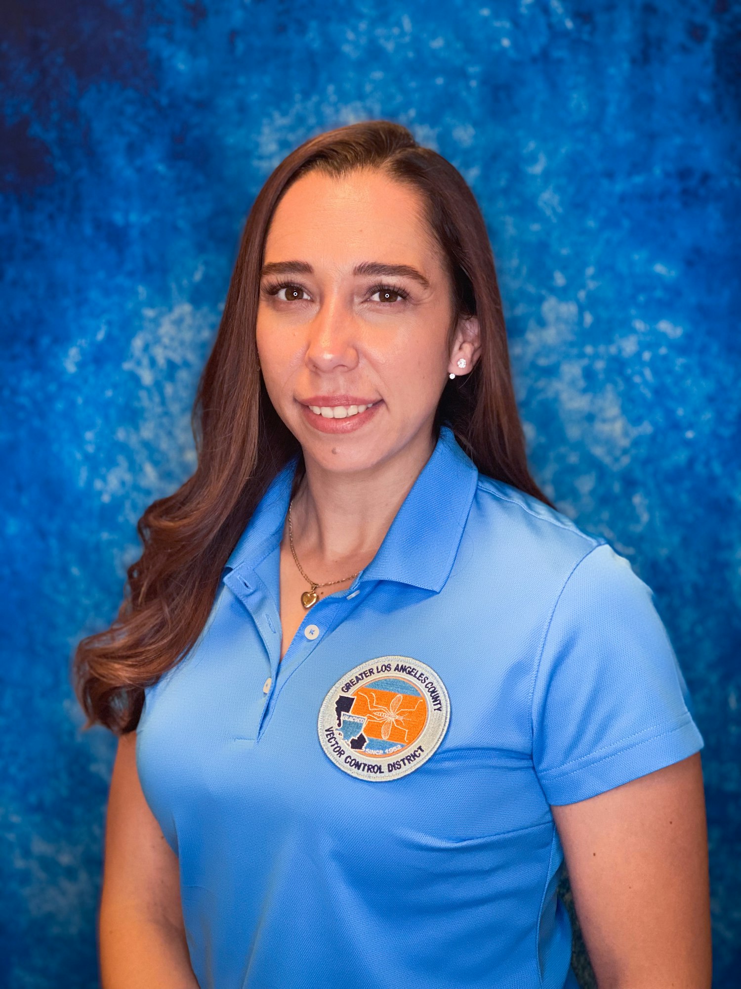 A woman in a blue polo shirt with a logo stands against a blue textured background.