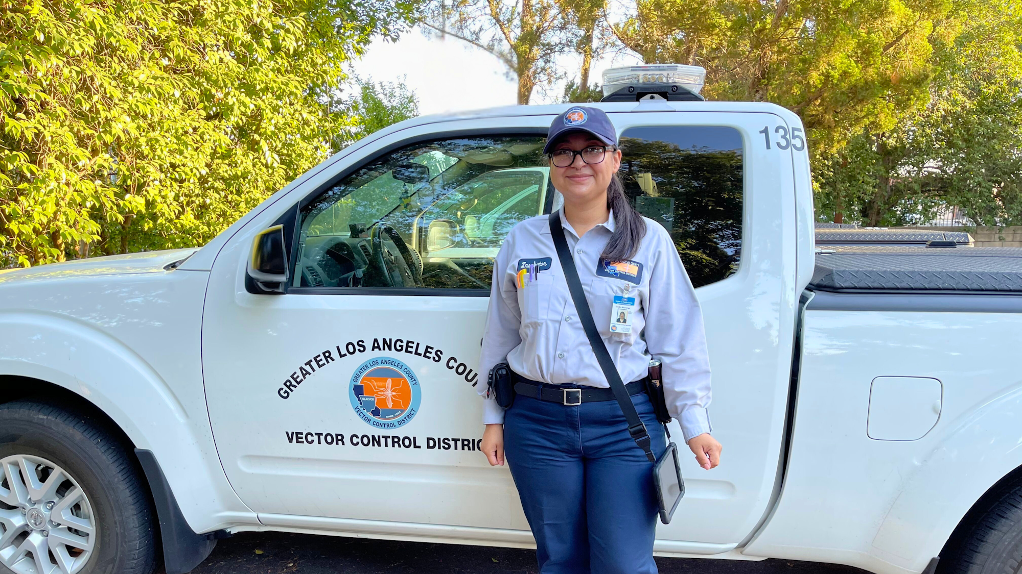 A person in uniform stands next to a Greater Los Angeles County Vector Control District vehicle.