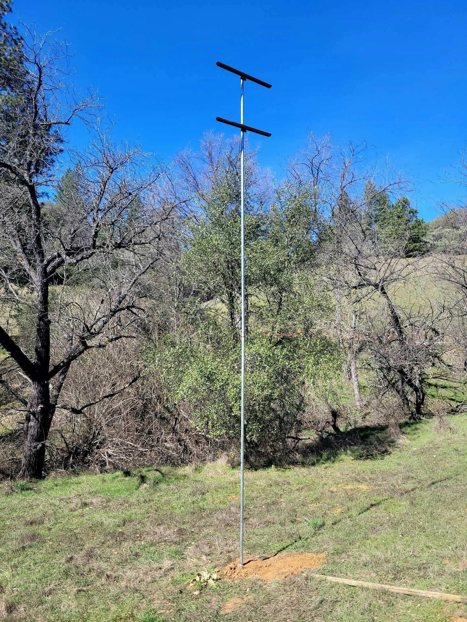 A tall metal pole with two horizontal bars on a grassy field with trees in the background.