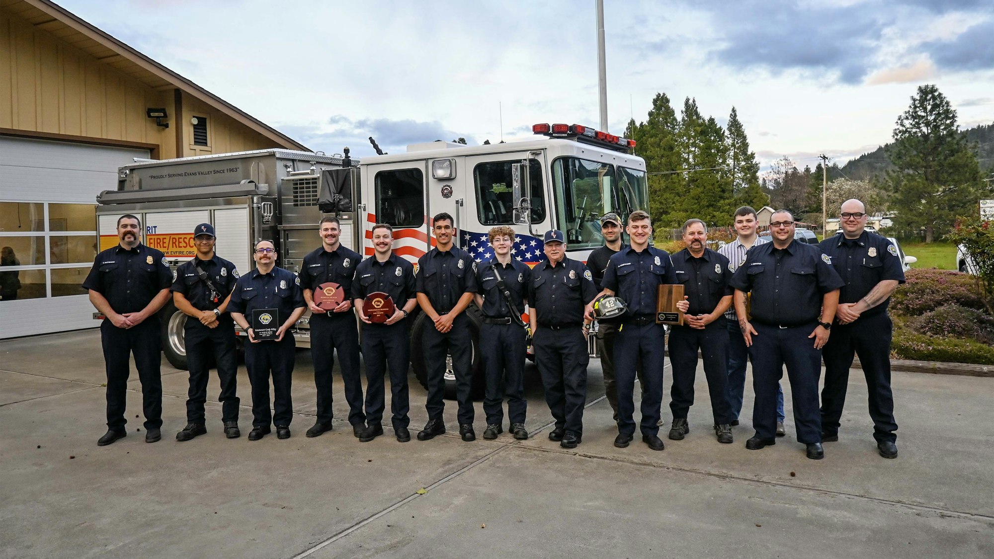 A group of firefighters posing with awards in front of a fire truck.