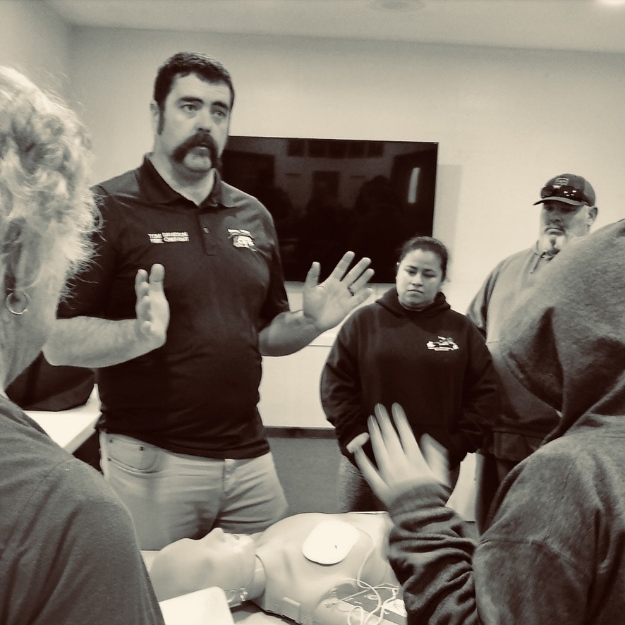 A group of people is engaged in CPR training with a practice dummy on the table.