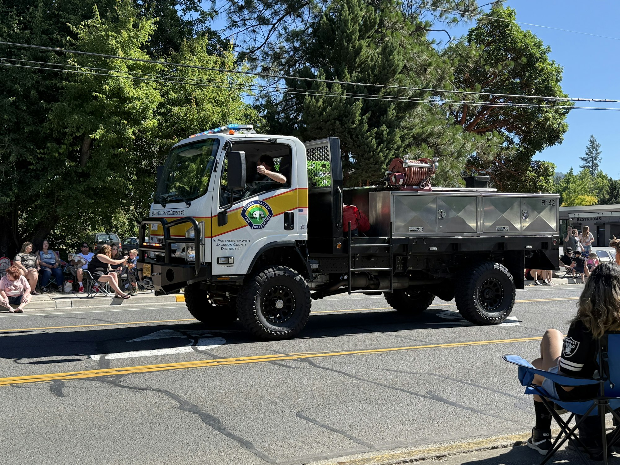A fire truck drives in a parade, with people seated along the street watching.