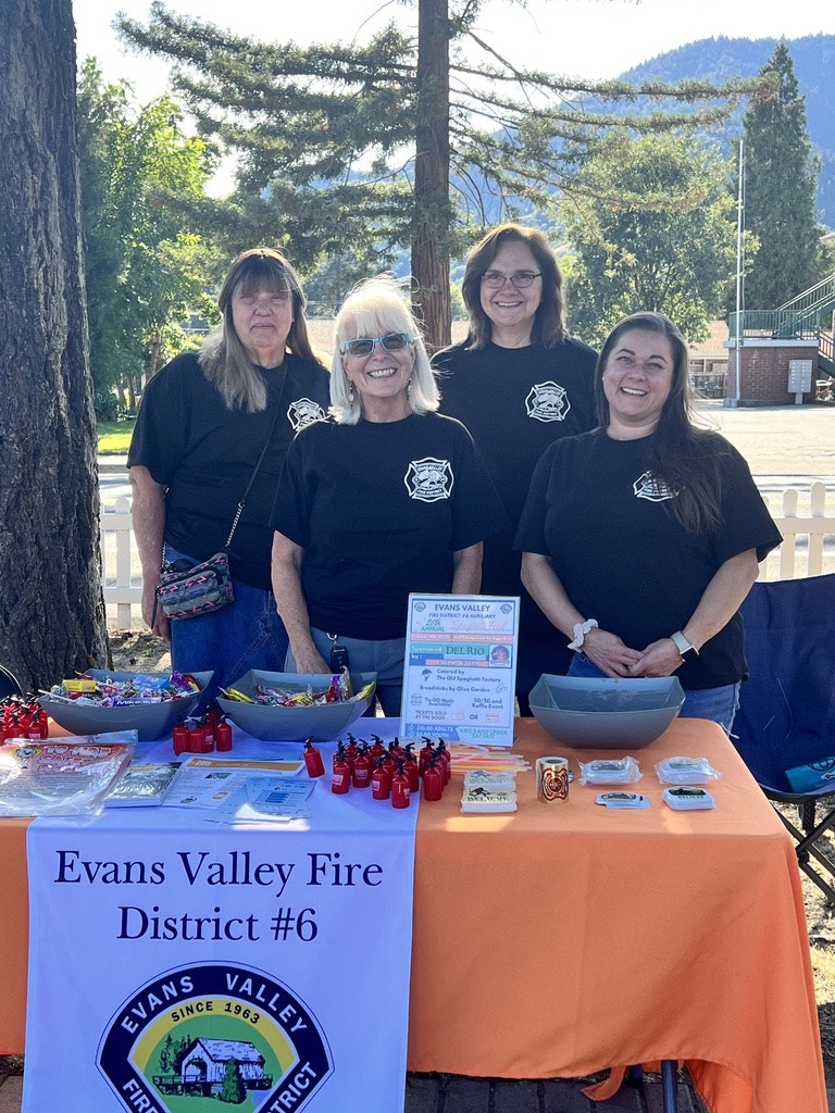 Four people in matching shirts stand behind a table for Evans Valley Fire District #6, displaying items and information.