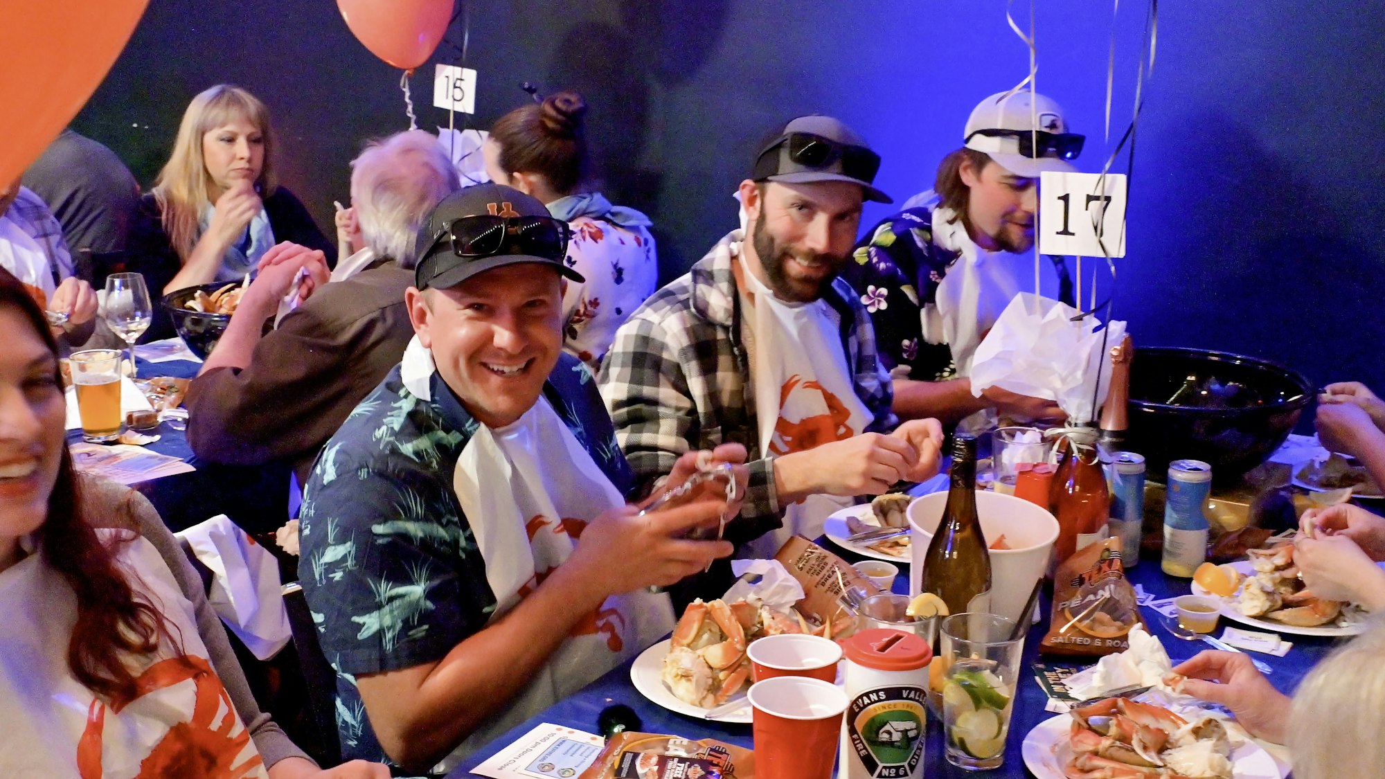 People at a table enjoying seafood with bibs, surrounded by drinks and balloons.