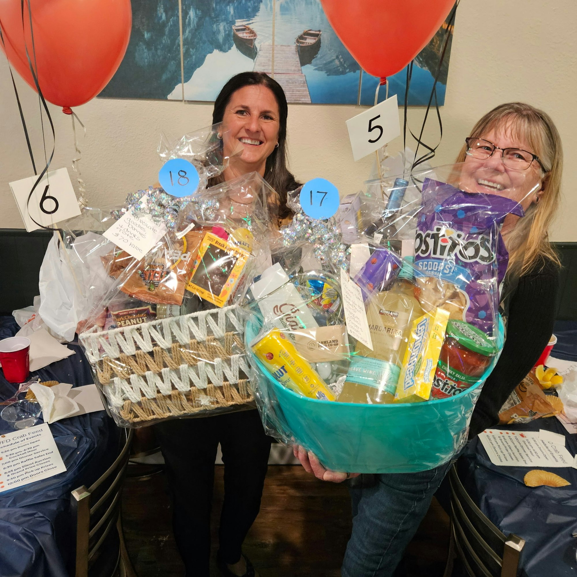 Two people holding gift baskets filled with snacks and items, with red balloons attached.