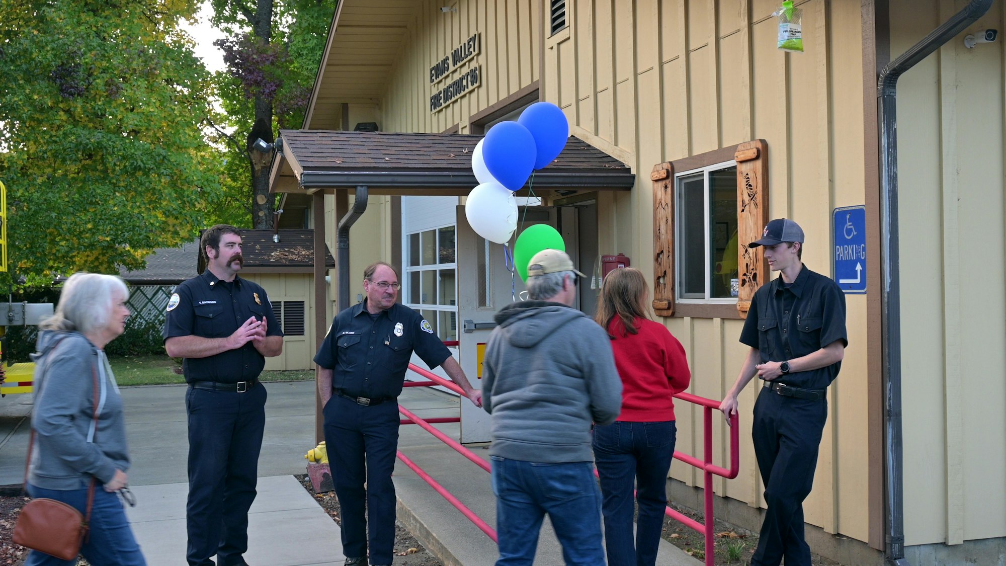 People gathering outside a fire station with balloons.