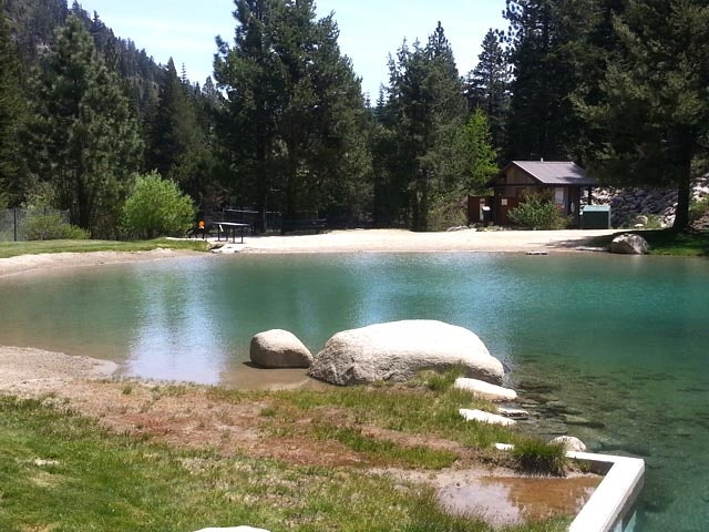 A serene pond surrounded by trees, a cabin, and rocks on the shore.