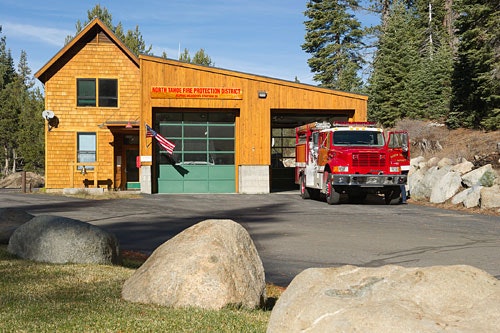 Fire station with a red fire truck, surrounded by trees and large boulders.