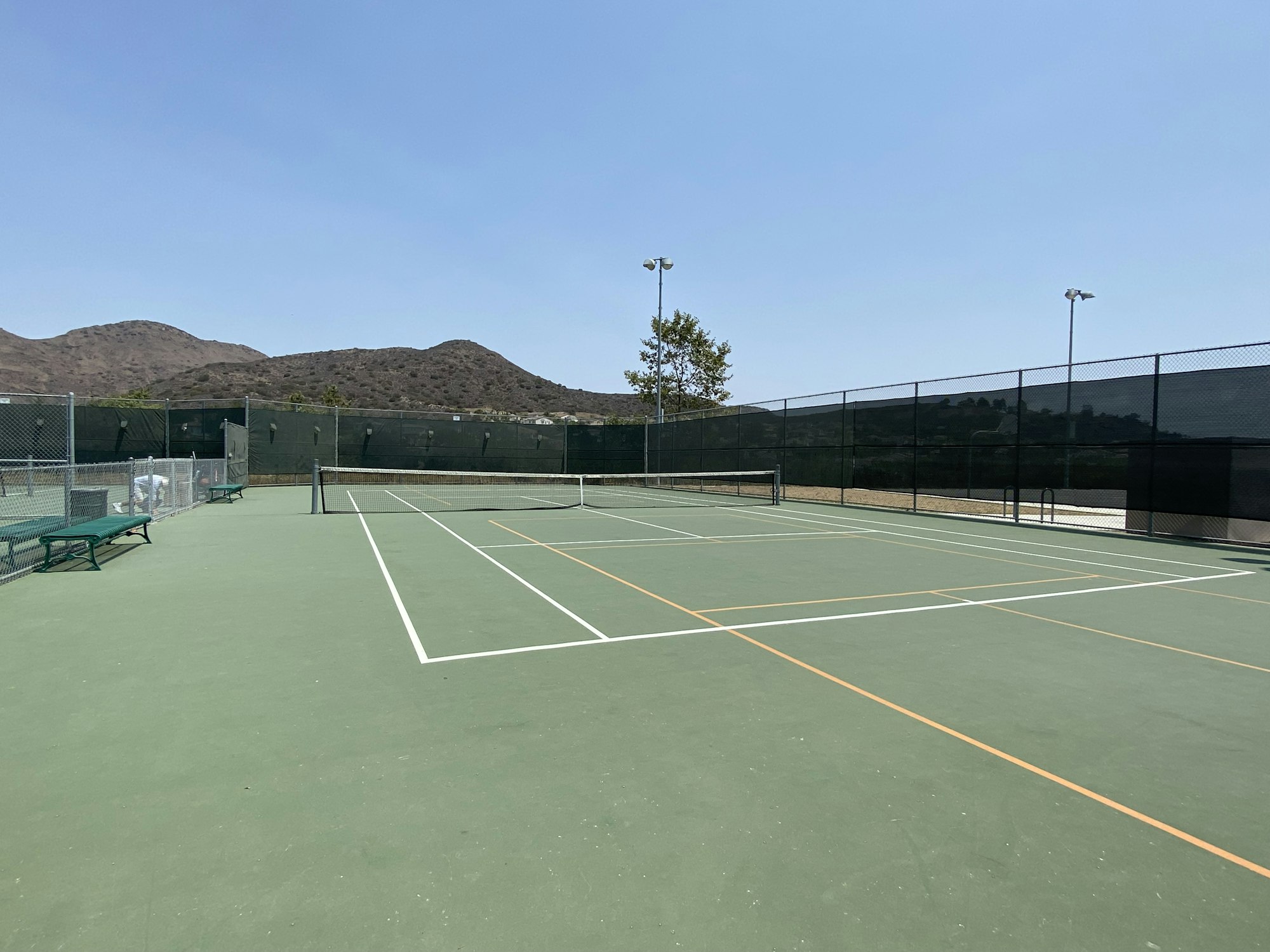 An empty outdoor tennis court with a mountain view in the background.