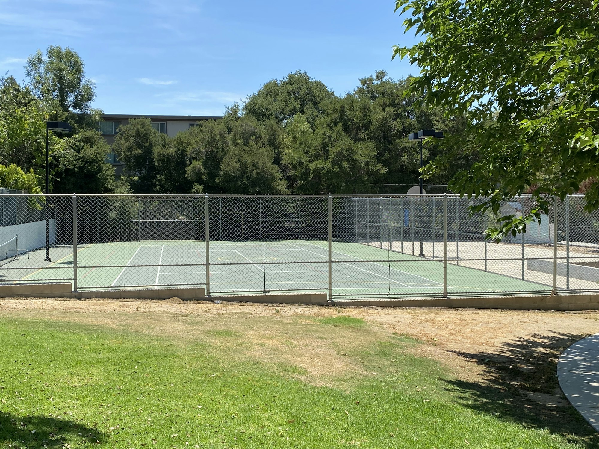 A fenced tennis court with trees and a building in the background.