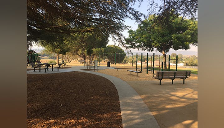 Outdoor playground with benches, swing sets, trees, and walking paths under clear skies.