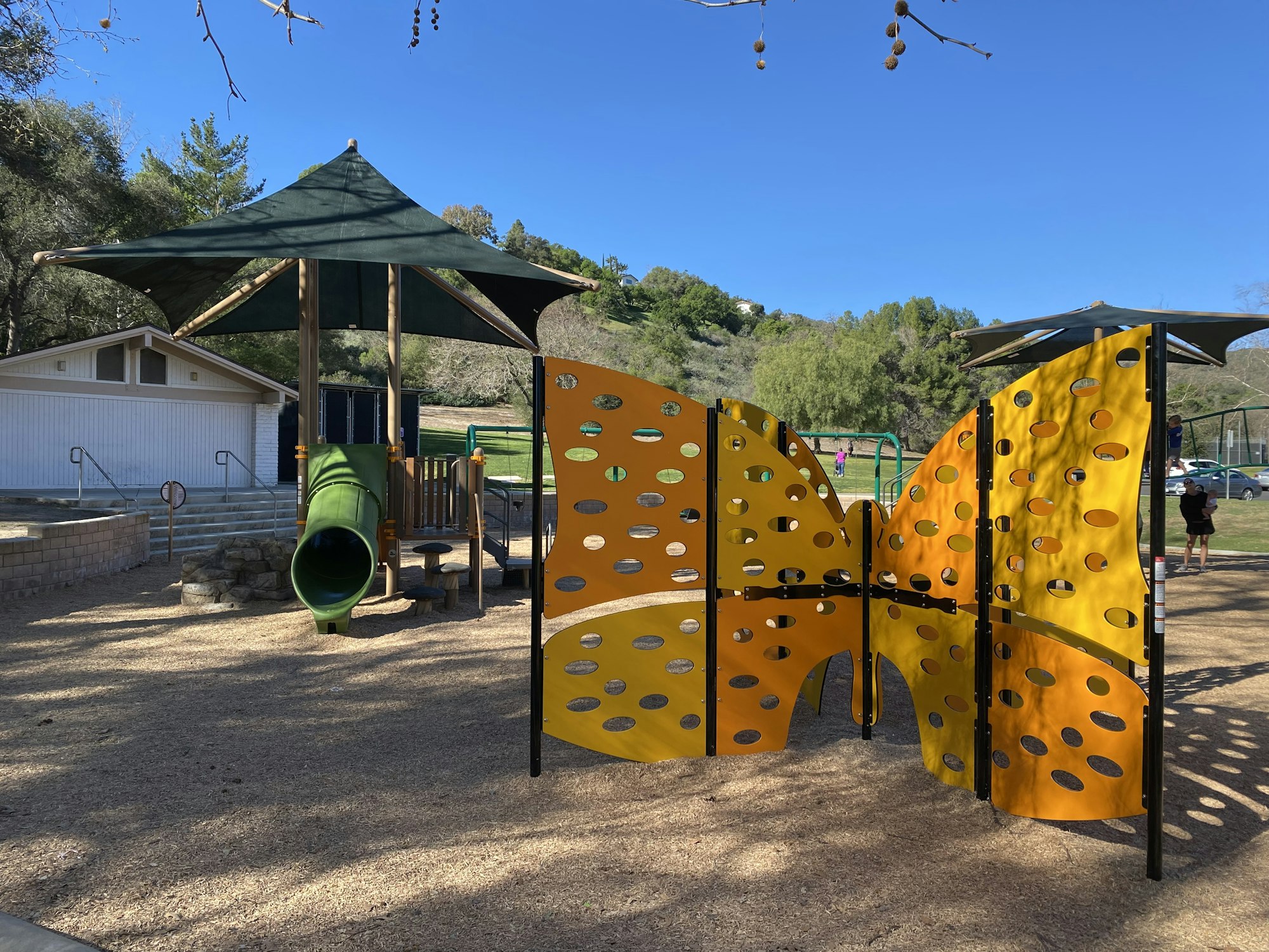 A playground with a slide, climbing structures, and shade canopies on a sunny day.