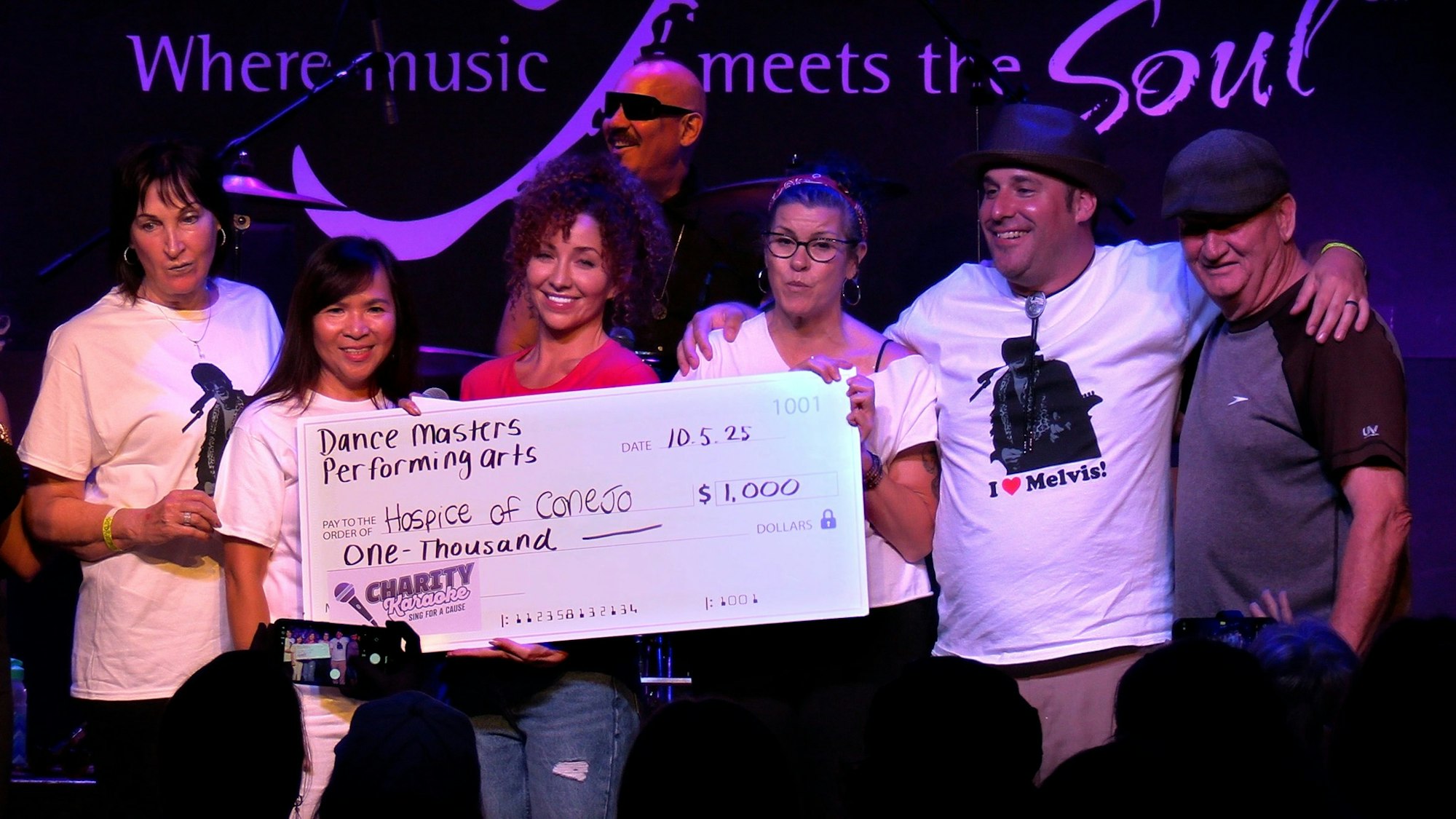People on stage holding a large check for $1,000 to "Hospice of Conejo" from "Dance Masters Performing Arts."