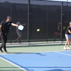 Two people playing pickleball on a court, one hitting the ball with a paddle.