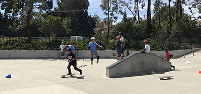 People skateboarding and socializing at a skate park surrounded by trees.