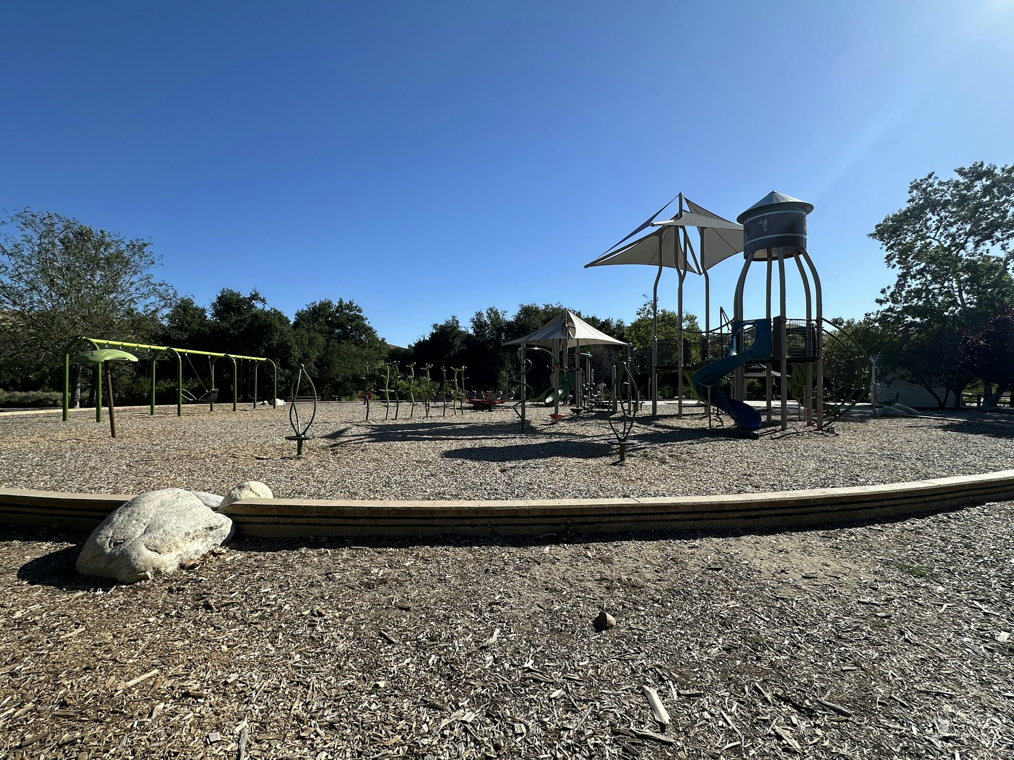A playground with swings, a slide, climbing structures, and a clear blue sky overhead.