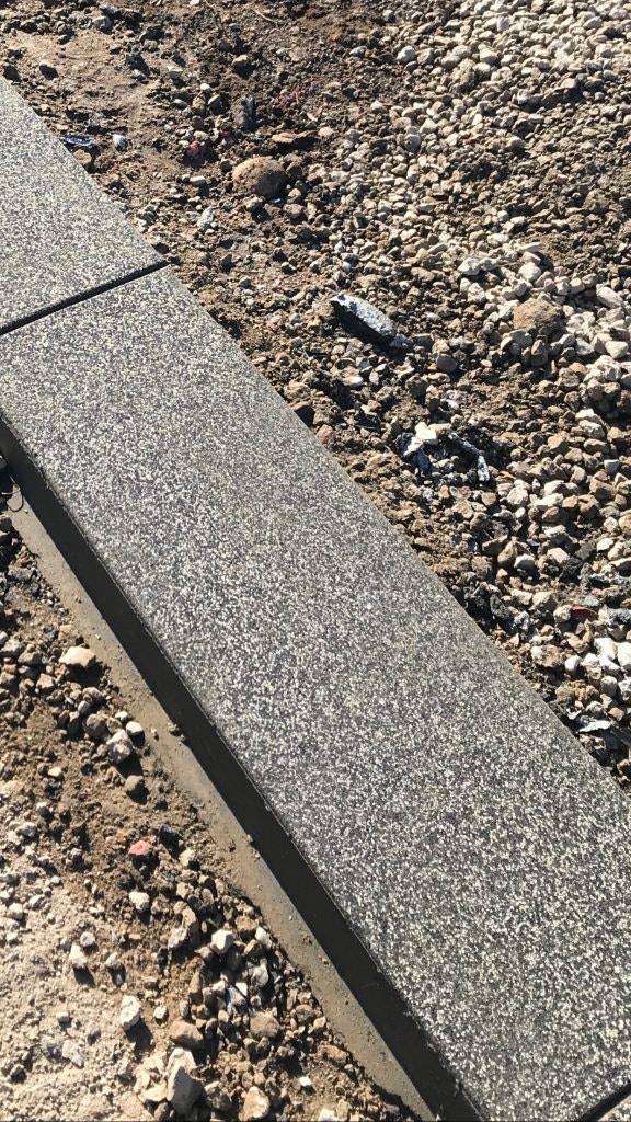 A newly installed concrete curb with gravel and dirt surrounding it.