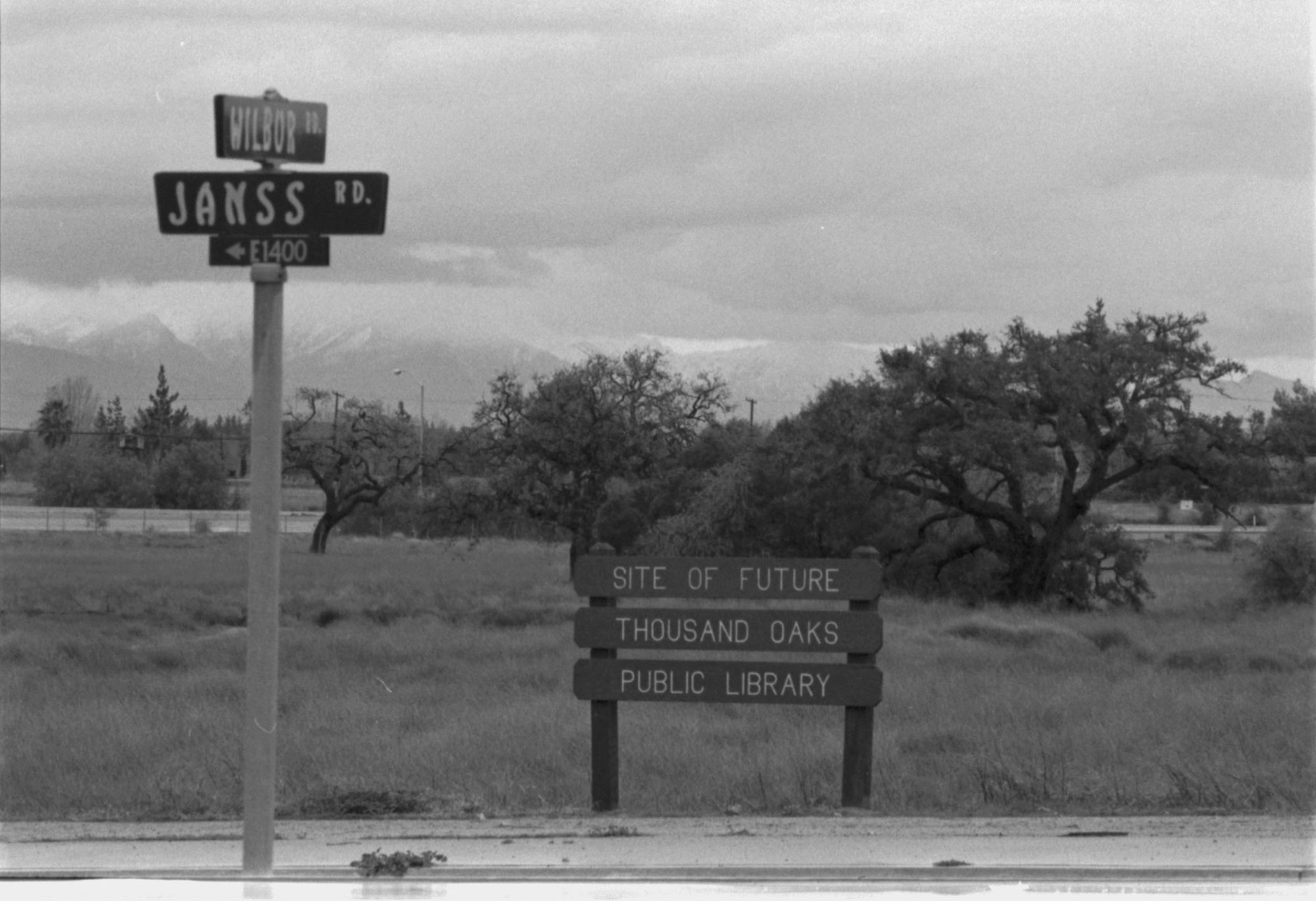 Street signs for Janss and Wilbur roads, grassy field, and a sign reading "Site of Future Thousand Oaks Public Library."