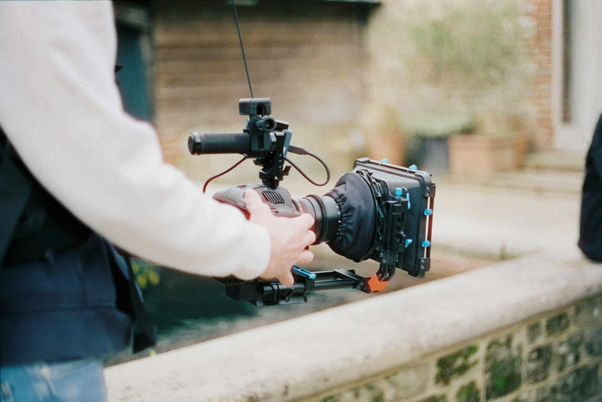 A person operating a professional camera with a microphone attached, outdoors.