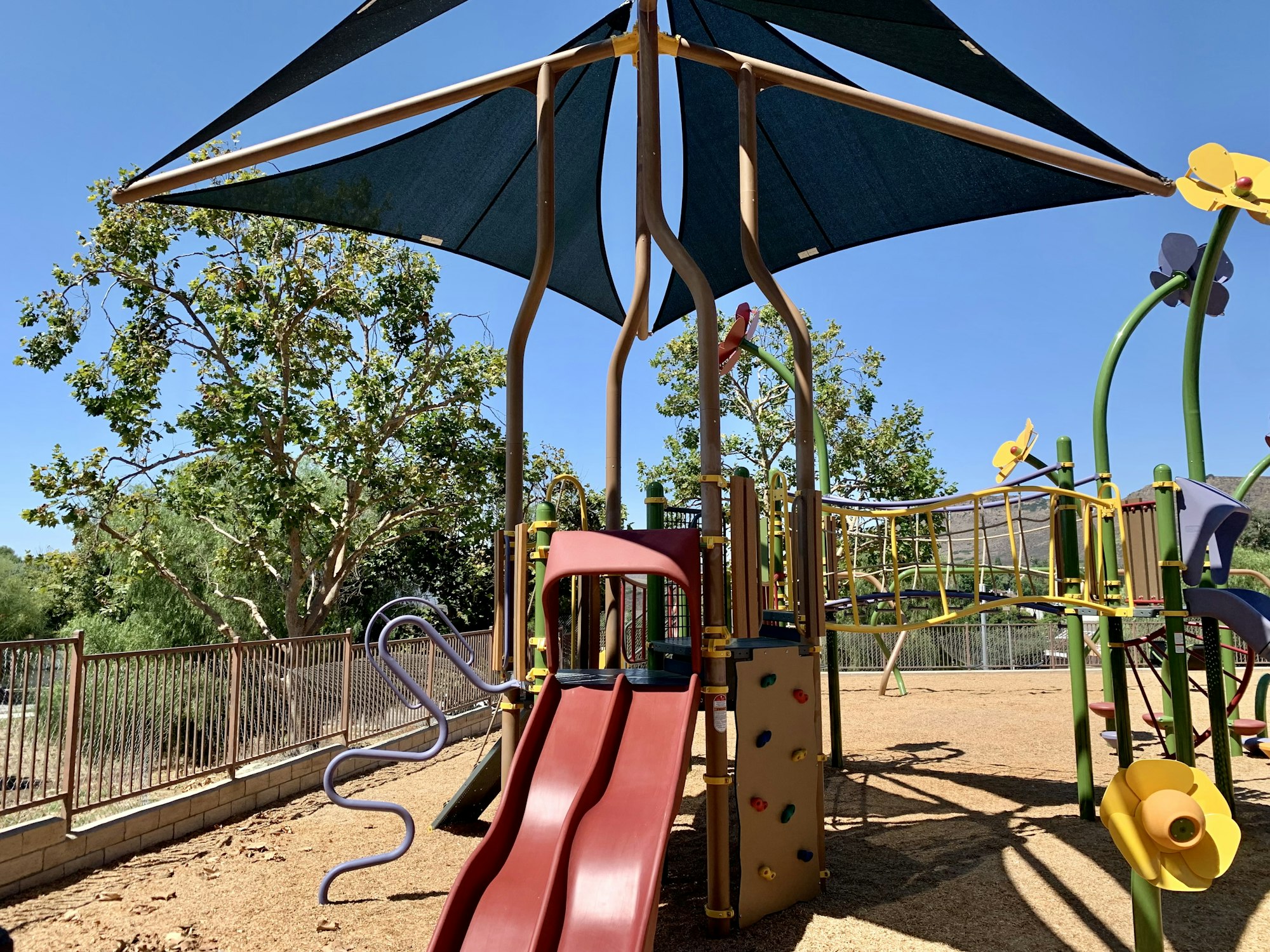 Playground with slides, climbing structures, and sun shades on a sunny day.