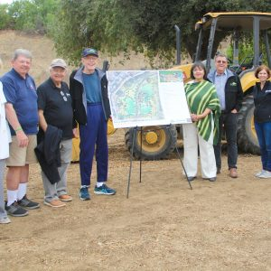 A group of people standing outdoors near a construction vehicle, looking at a map on a stand.