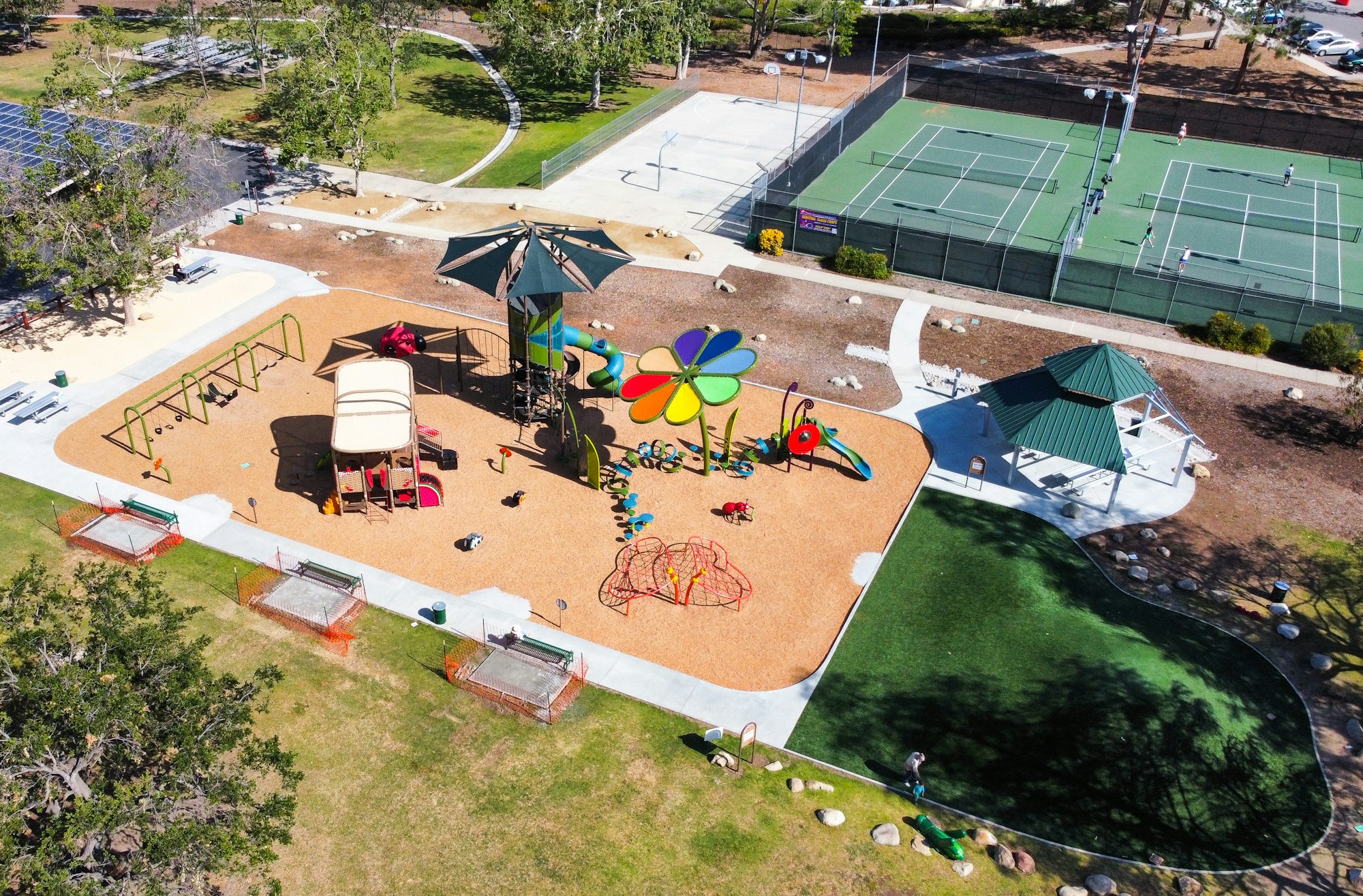 Aerial view of a park with a playground, picnic area, basketball court, and tennis courts.