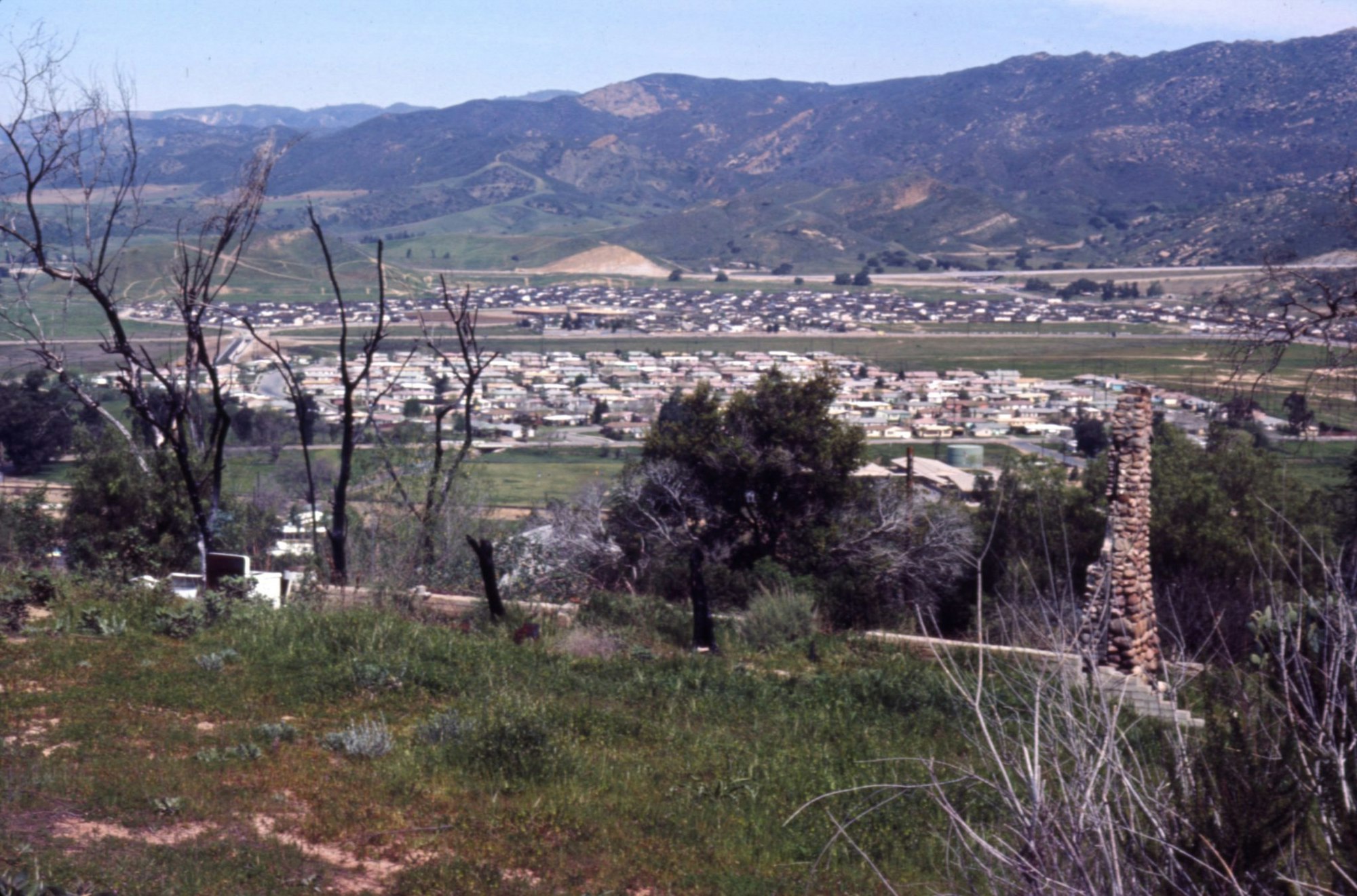 A hillside view of a town with many houses, surrounded by green fields and mountains in the background.