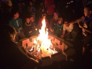 People gathered around a campfire at night, wearing glow necklaces.