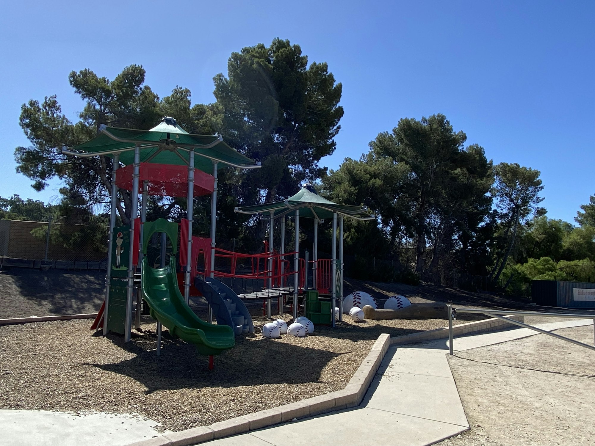 Playground with slides and canopy roofs, surrounded by trees and walking paths.