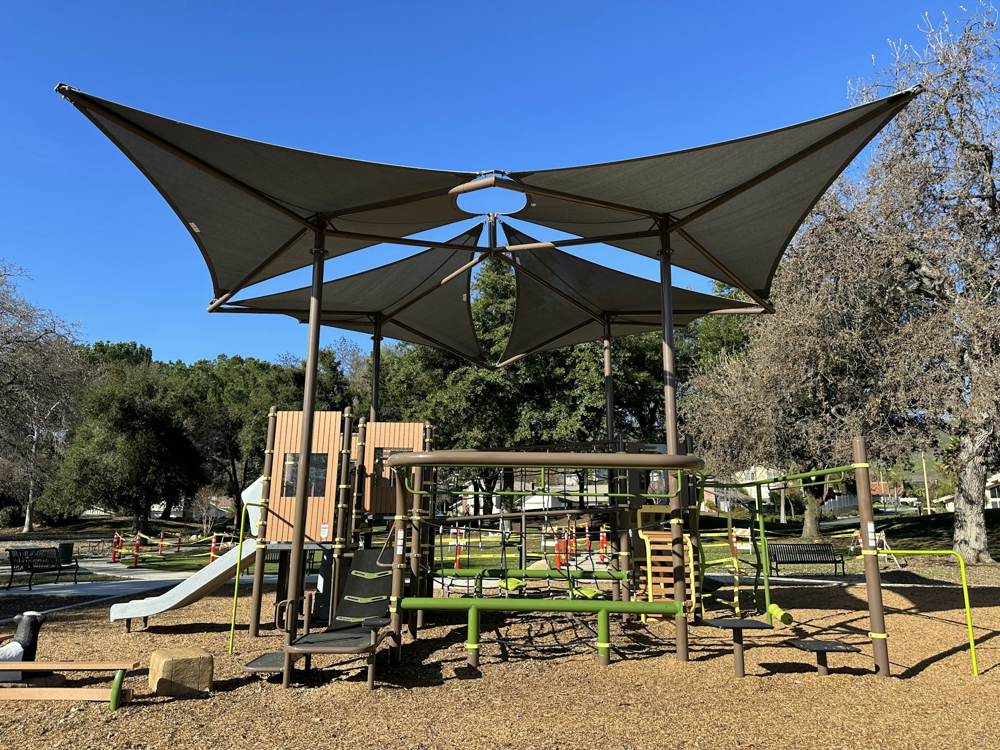 Children's playground with climbing structures, slides, and shade canopies under a clear blue sky.