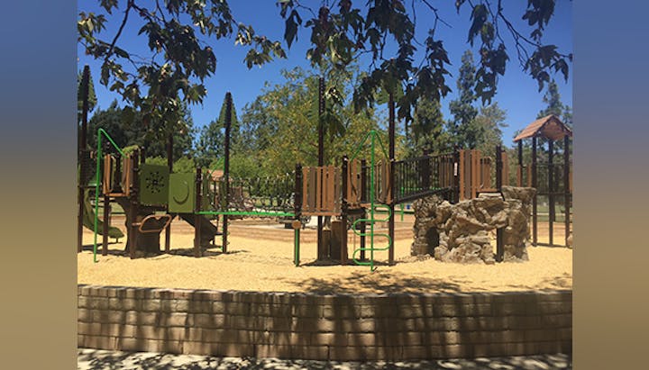 Playground with slides, climbing structures, and wood chips, surrounded by trees under a clear blue sky.