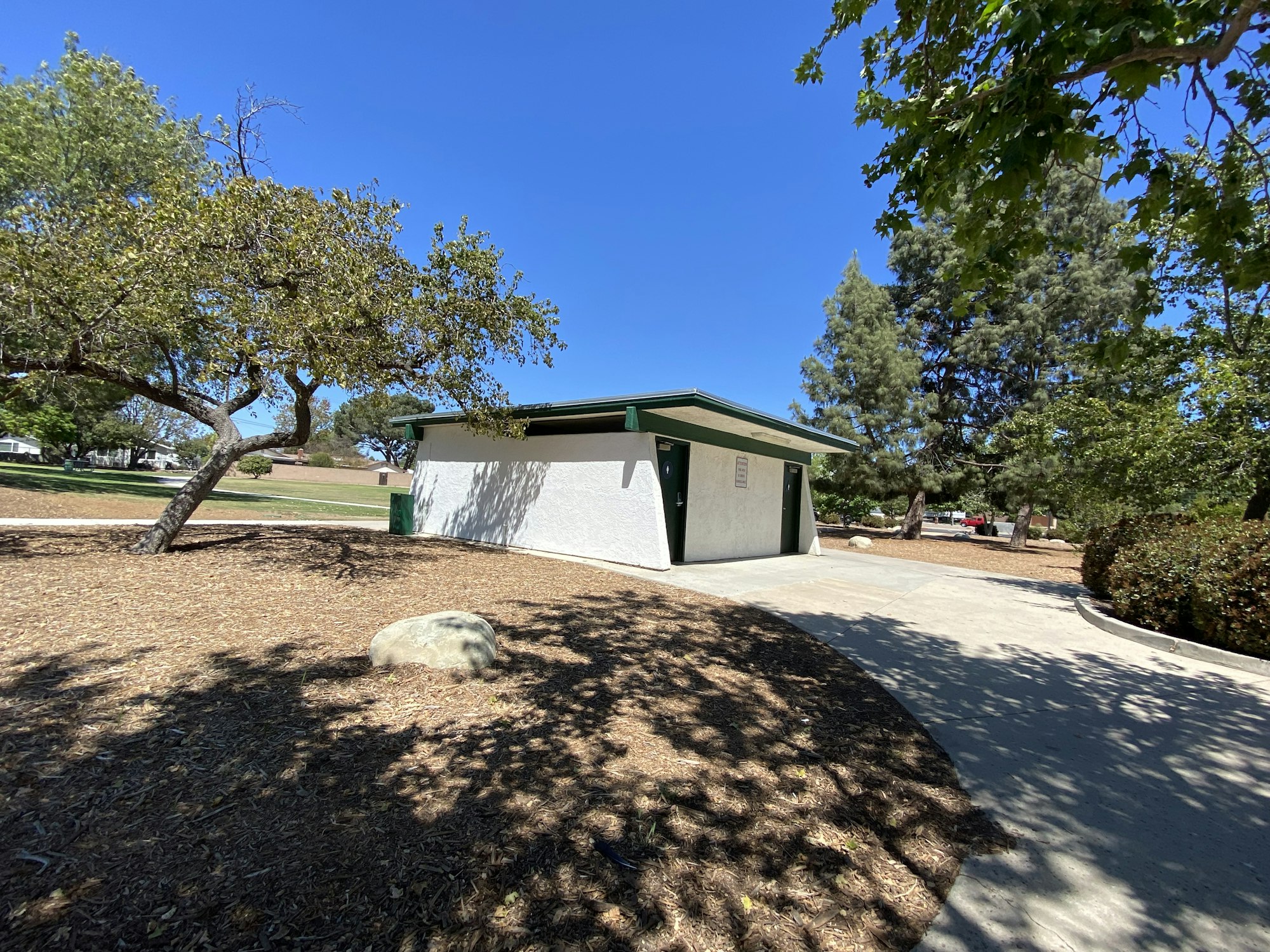 Small park restrooms surrounded by trees and a clear blue sky.
