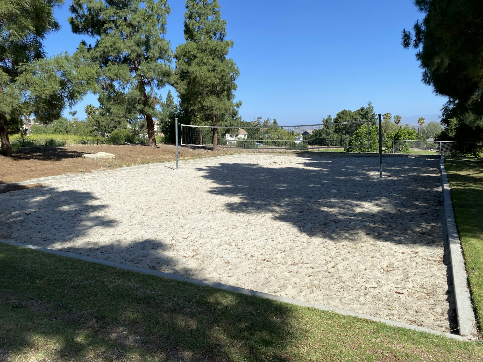 A sand volleyball court with a net, surrounded by trees and grass.