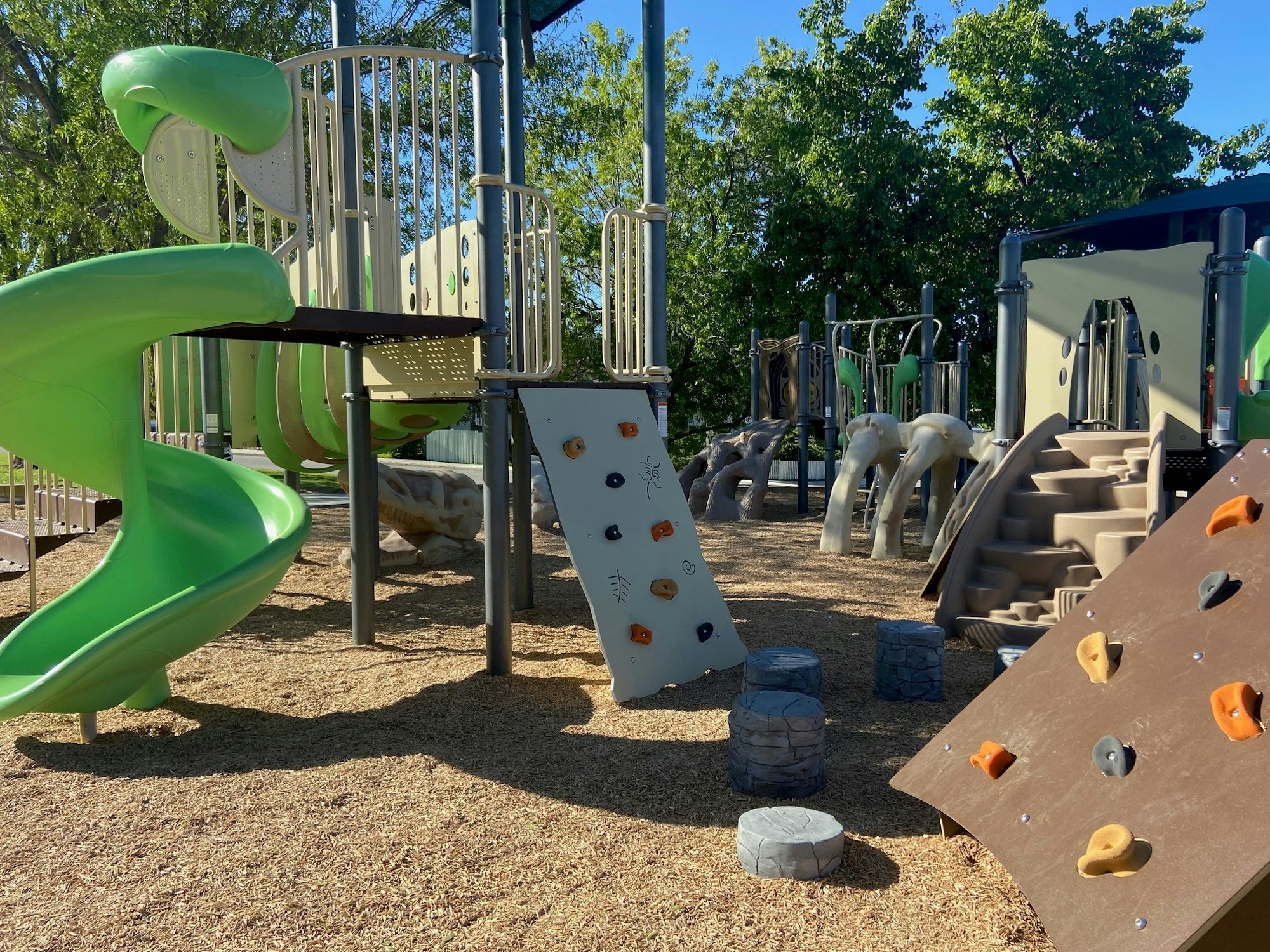 Playground with climbing structures, slides, and stepping stones under a clear blue sky.