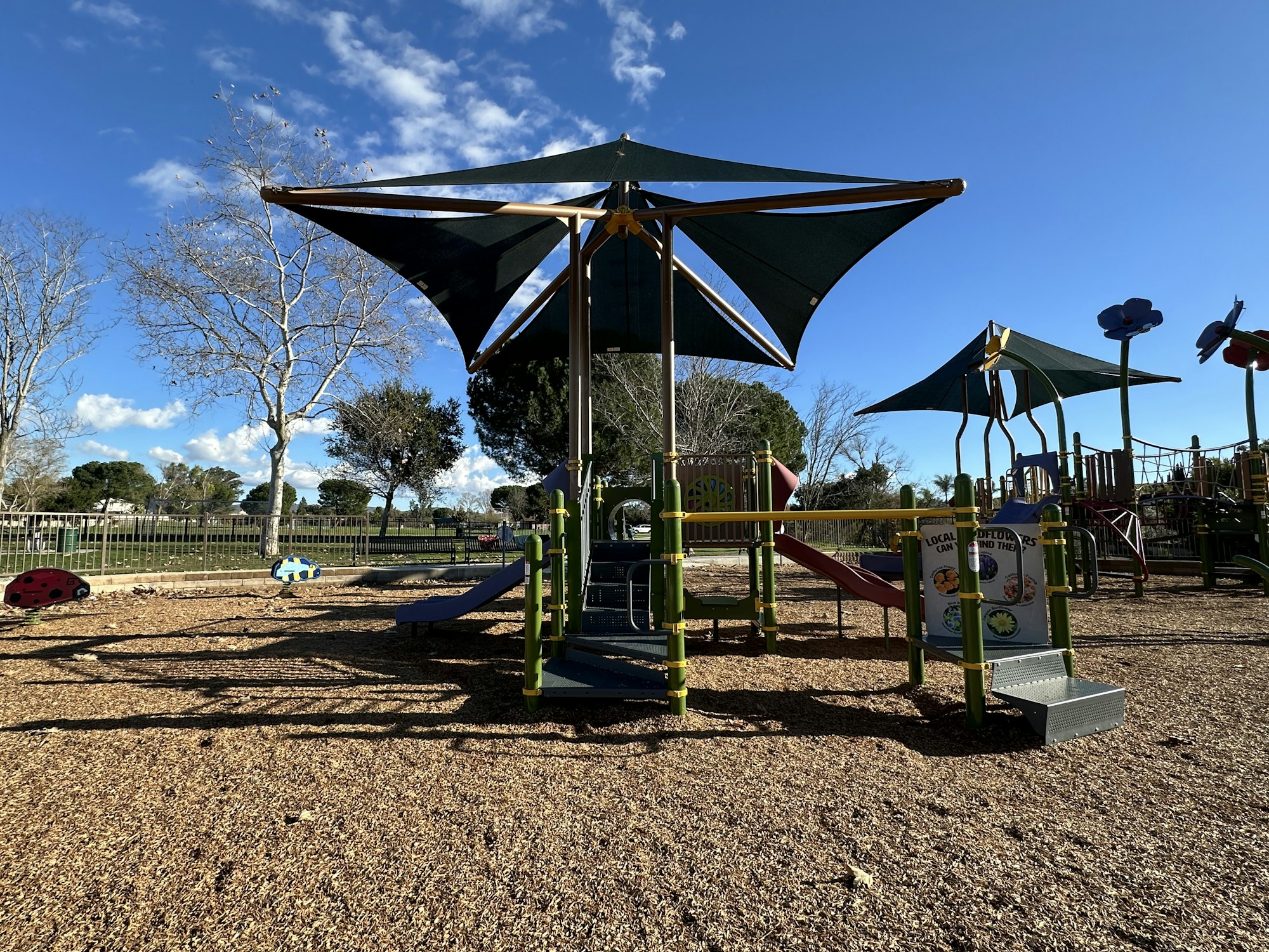 Playground with slides, climbing structures, and shade canopies on a sunny day.