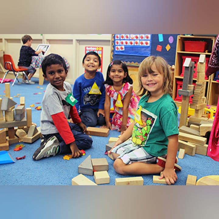 Four children smiling and playing with wooden blocks in a colorful room.