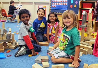 Four children smiling and playing with wooden blocks in a colorful room.