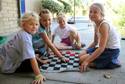 Four children are sitting on the ground playing a game of checkers outdoors.
