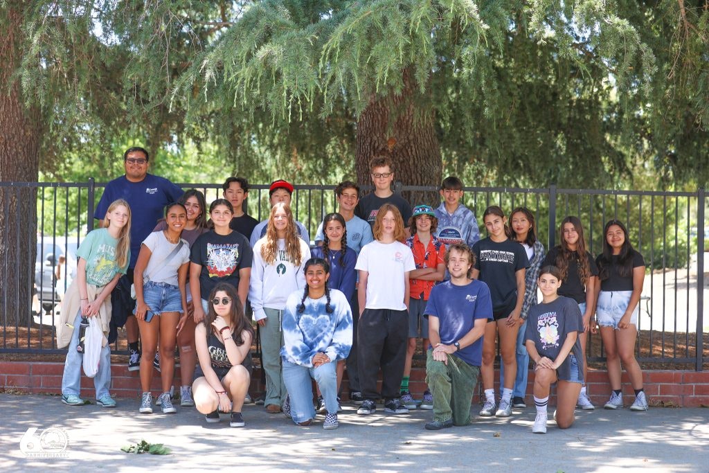 A group of people posing outdoors, in front of trees and a fence.