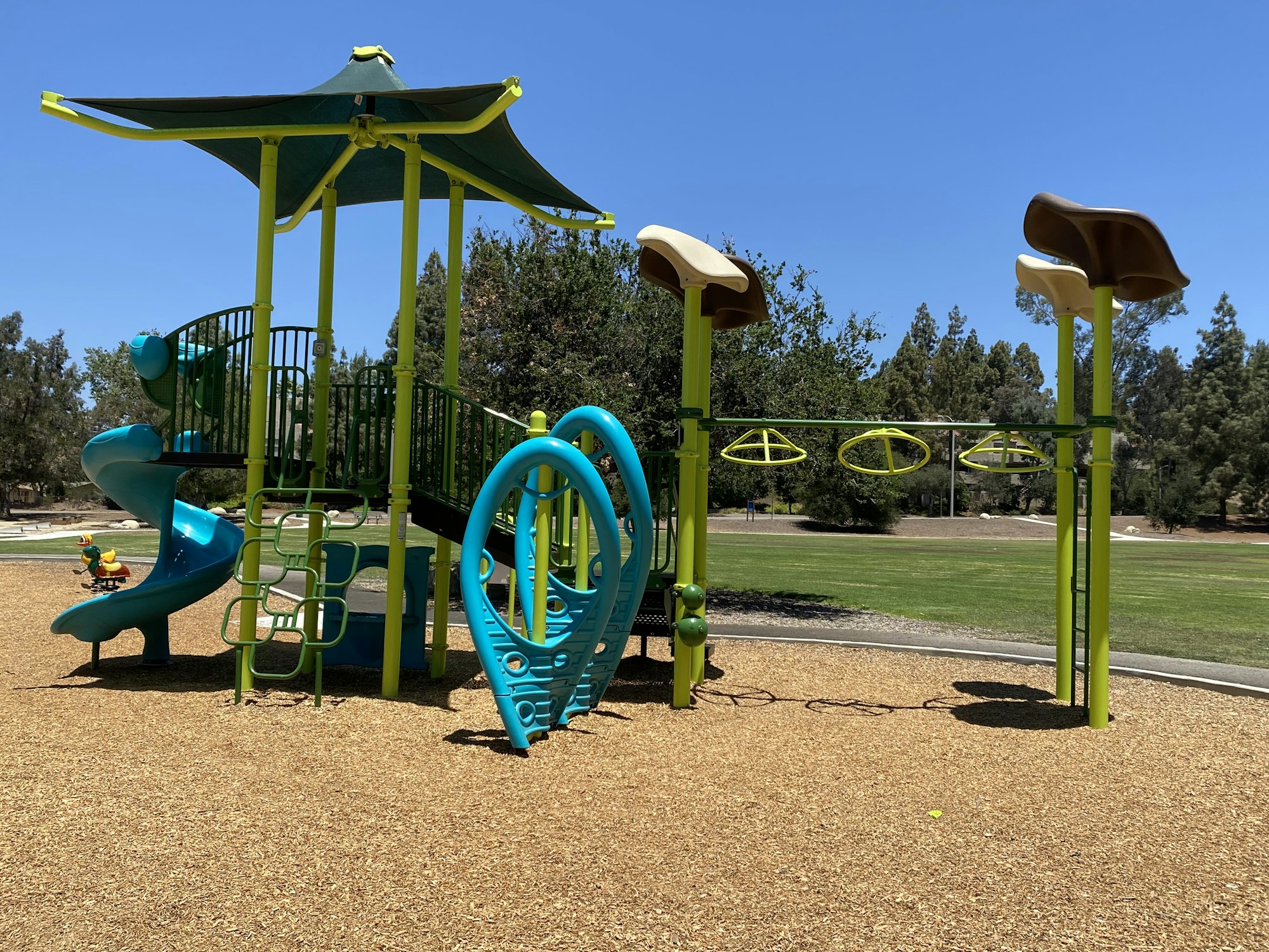 Children's playground with slides, climbing structures, and swings on a sunny day in a park.