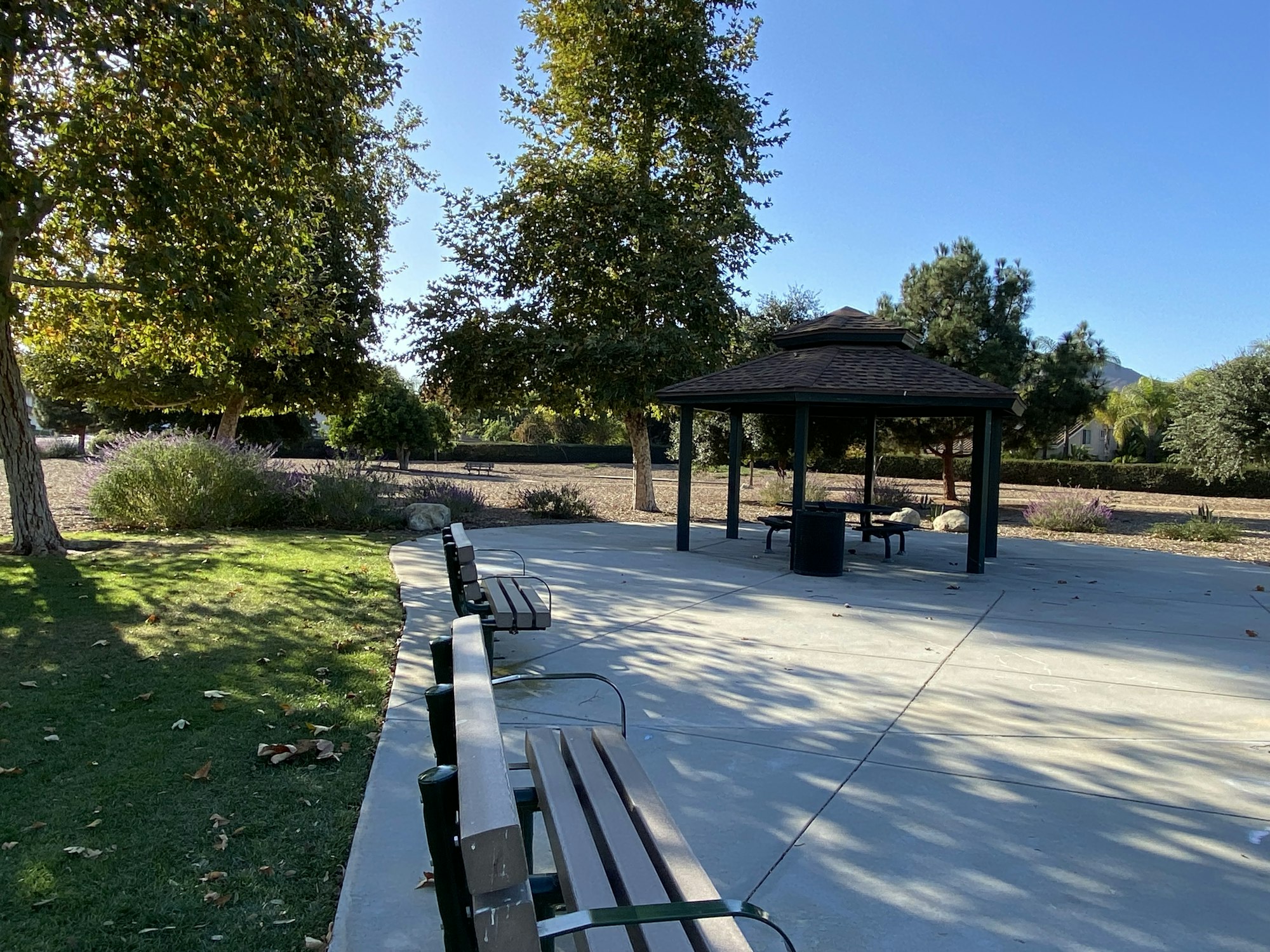A park with benches, a gazebo, and trees under a clear blue sky.