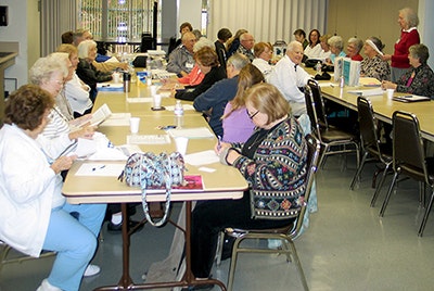 A group of seniors seated at tables in a classroom setting, engaged in a lecture or discussion.