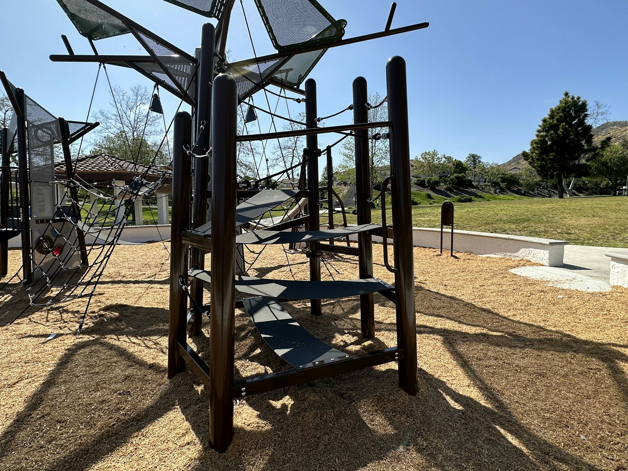 Playground climbing structure with nets and platforms on a sunny day.